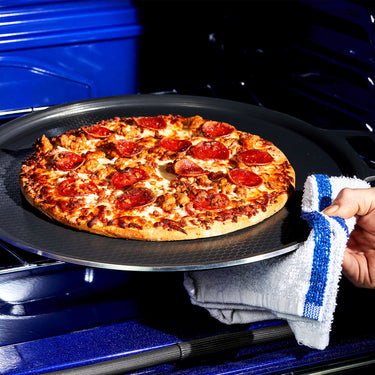 A hand taking a pepperoni pizza out of the oven on the HexClad hybrid pizza steel
