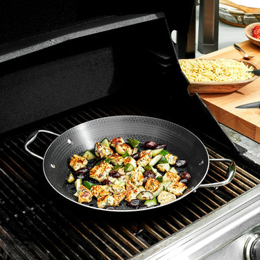 Pieces of chicken and vegetables being cooked in the HexClad 12" Hybrid BBQ Grill Pan on top of a grill