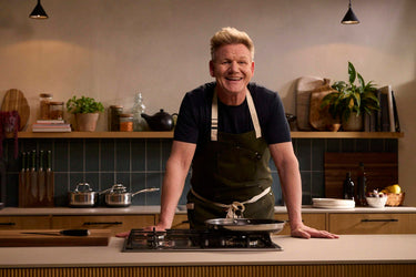 Chef Gordon Ramsay smiling, standing at a kitchen counter.	