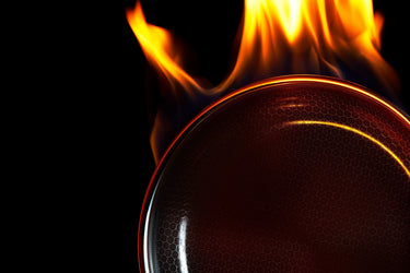 A studio image of a HexClad pan, with flames coming from the top of it.