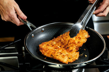 Someone flipping a chicken cutlet in a pan, using tongs.
