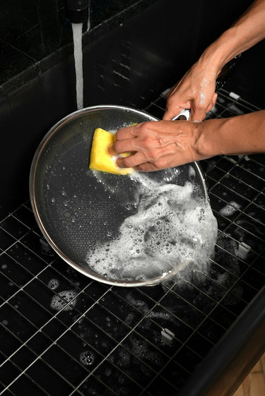 Someone cleaning a HexClad nonstick pan with a soapy sponge and water.