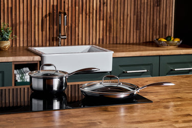 A HexClad saucepan and frying pan, both with lids, placed on an induction cooktop in a modern kitchen.