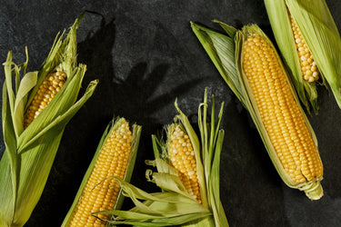 5 ears of corn on a black countertop surface.