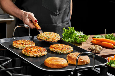 A person making chicken burgers on the HexClad Hybrid Double Burner Griddle.