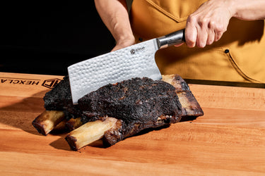 A person slicing cooked ribs with a cleaver.