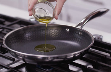A person pouring a small amount of oil into a HexClad carbon steel pan.