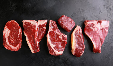 Various cuts of steak lined up together on a black surface.