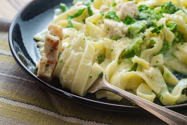 A plate of fettuccine alfredo, served with broccoli and chicken.