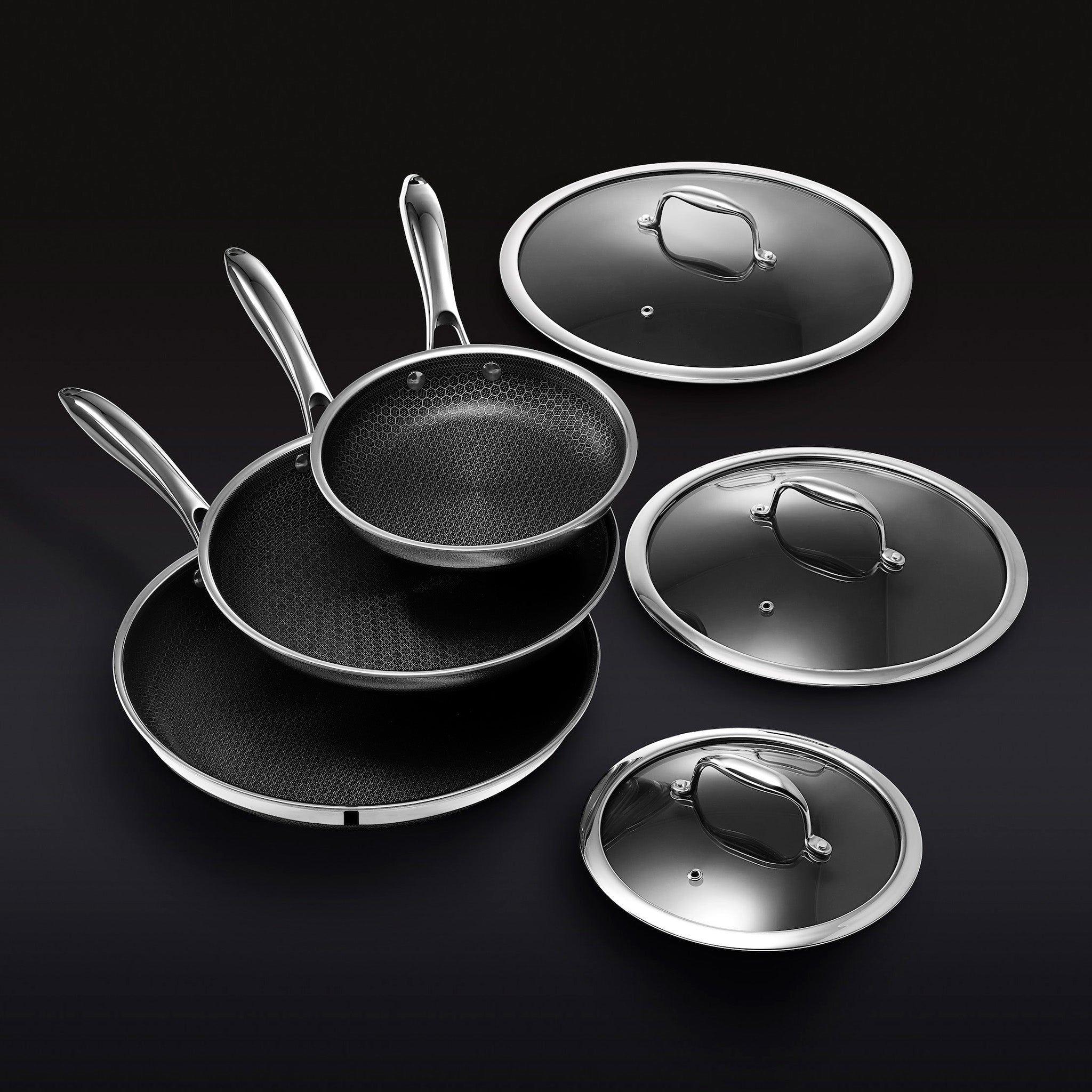 Three non-stick frying pans with lids on a black background.